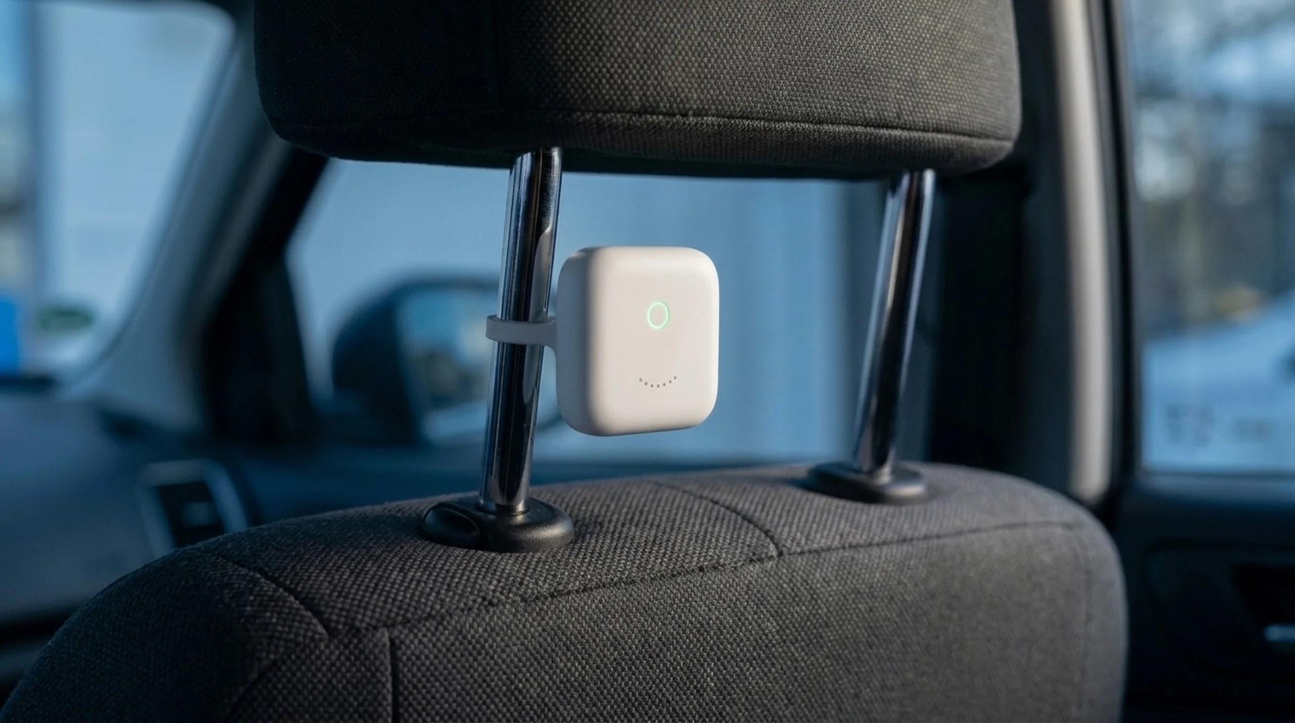 The Sensor clipped to the posts of a car headrest, its ring glowing mint.